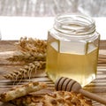 A jar of liquid honey stands on a wooden table next to cookies and wheat ears