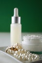 A jar of luxury beauty face cream and serum bottle with pearls on emerald green color background with copy space. Royalty Free Stock Photo