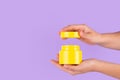 Jar of moisturizing facial cream. Yellow plastic container with cream vitamin c on purple background. Yellow unbranded, balsam,