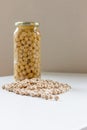 Jar of non-perishable cooked chick peas with dried chick peas spilled in front of it