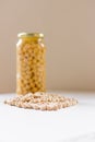 Jar of non-perishable cooked chick peas with dried chick peas spilled in front of it