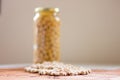 Jar of non-perishable cooked chick peas with dried chick peas spilled in front of it