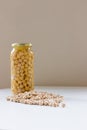 Jar of non-perishable cooked chick peas with dried chick peas spilled in front of it