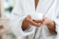 Jar of nourishing cream in hands of unrecognizable black woman in bathrobe