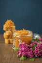 A jar of orange confiture and pieces of French baguette and red flowers on the sackcloth and wooden background