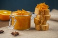 A jar of orange confiture and pieces of French baguette with star anise on the sackcloth and wooden background