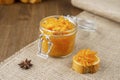 A jar of orange jam and piece of French baguette with star anise on the sackcloth and wooden background