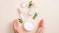 Jar of organic hand cream, essential oils bottle and green leaves on beige background. Skin care, organic natural beauty products