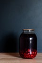 Jar of raspberry and cherry juice on the wooden table in front of black wall Royalty Free Stock Photo