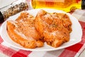 Jar with spices, bottle of vegetable oil, raw pieces of fillet turkey in white plate on checkered napkin Royalty Free Stock Photo