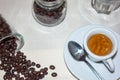 Jar with spilled coffee beans on linen tablecloth with cup of espresso full with spoon.