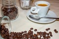 Jar with spilled coffee beans on linen tablecloth with cup of espresso full with spoon.