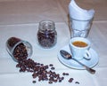 Jar with spilled coffee beans on linen tablecloth with cup of espresso full with spoon Royalty Free Stock Photo