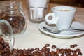 Jar with spilled coffee beans on linen tablecloth with cup of espresso full with spoon. Royalty Free Stock Photo