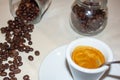 Jar with spilled coffee beans on linen tablecloth with cup of espresso full with spoon. Royalty Free Stock Photo