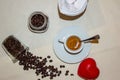 Jar with spilled coffee beans on linen tablecloth with cup of espresso full with spoon.