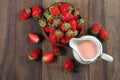 Jar with strawberry milk, ripe strawberries in a wooden bowl on a wooden table. top view