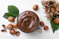 Jar with tasty chocolate spread, hazelnuts and green leaves on white wooden table, flat lay Royalty Free Stock Photo