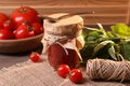 Jar of tasty tomato paste with spoon, ingredients and thread on wooden table