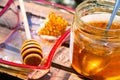 A jar of thick golden honey with a spoon, a wooden honey dipper in a glass plate and a piece of honeycomb. Harvesting