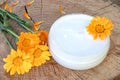 A jar of white cosmetic cream for body care. Fresh orange calendula flowers on wooden background Royalty Free Stock Photo