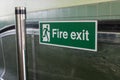Green fire exit sign on glass panel on metal pole at top of escalator