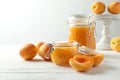 Jars of apricot jam and fresh fruits on white wooden table
