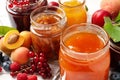 Jars with different jams and fresh fruits on white wooden table, closeup Royalty Free Stock Photo