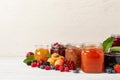 Jars with different jams and fresh fruits on white wooden table. Space for text Royalty Free Stock Photo