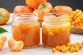 Jars of sea buckthorn and tangerine jam. Plate of sea buckthorn berries and mandarin oranges fruits on background