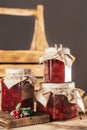 Jars of homemade lingonberry and pear jam with craft paper on lids on wooden table next to fresh lingonberries. Vertical