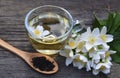 Jasmine tea in a glass cup with dry green leaves in a spoon and fresh jasmin flowers on old wooden table. Royalty Free Stock Photo