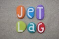 Jet Lag, creative text composed with hand painted multi colored stone letters over beach sand