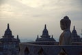 Amazing sunrise view of meditating Buddha statue and stone stupas. Ancient Borobudur Buddhist temple Royalty Free Stock Photo