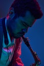 Jazz in modern music. Close up photo of young handsome man playing saxophone in neon light. Gel portraits.
