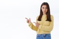 Jealous pouting offended cute sulky girlfriend in yellow sweater, frowning and looking insulted as pointing finger left