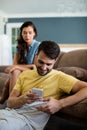 Jealous woman watching man using mobile phone in the living room Royalty Free Stock Photo