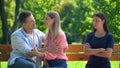 Jealous young woman looking at loving couple sitting park bench, resentment