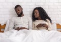 Jealous man peeking into wife`s cellphone sitting on bed together Royalty Free Stock Photo