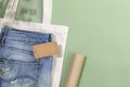 Jeans with empty craft label, textile bag and packing paper on green background