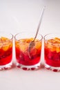 Jelly dessert with fruits apricot raspberry in three drinking glasses with single spoon yellow red summer white background in row