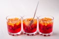 Jelly dessert with fruits apricot raspberry in three drinking glasses with single spoon yellow red summer white background in row