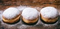 Krapfen with powder sugar, three and isolated on wooden background.