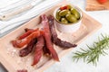 Jerky meat strips with spices, green olives, rosemary on wooden plate Royalty Free Stock Photo