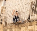 A child from a family of believers sits outside the window, on a decorative iron protective carved lattice and looks at passers-by