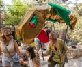 A festival participant in medieval dress walks between visitors with a large dragon in his hands at the Knights of Jerusalem