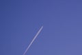 Jet airliner plane flying at high altitude leaves vapor trail / contrail against dark blue sky Royalty Free Stock Photo