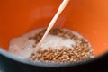 A jet of white milk is poured into a deep bowl of buckwheat.