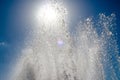 Jets and drops of water of the fountain on the background of the sun and blue sky with sun flare Royalty Free Stock Photo