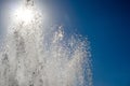 Jets and drops of water of the fountain on the background of the sun and blue sky with sun flare Royalty Free Stock Photo